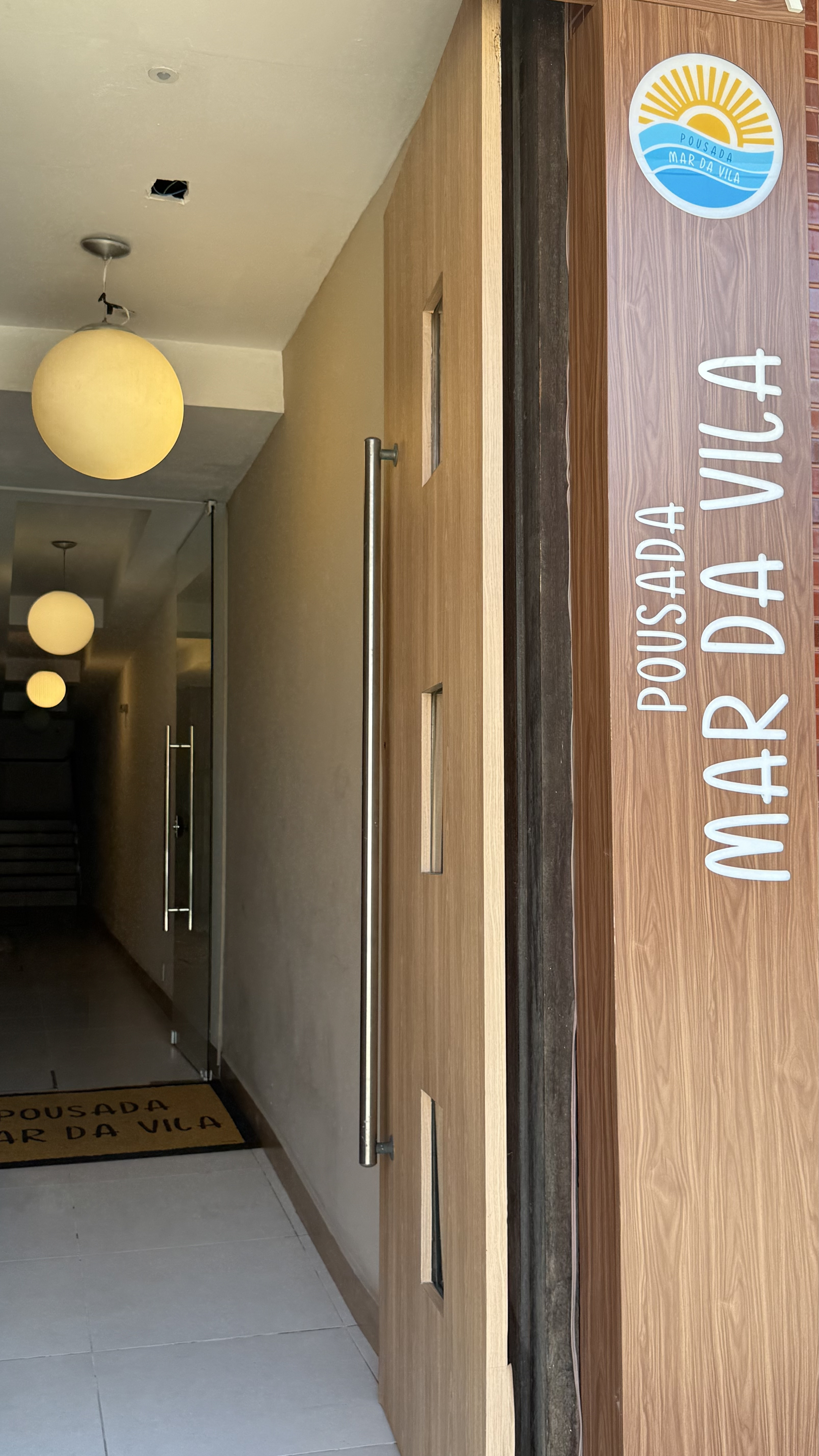 Entrada da Pousada Mar da Vila com logo na porta principal e corredor iluminado